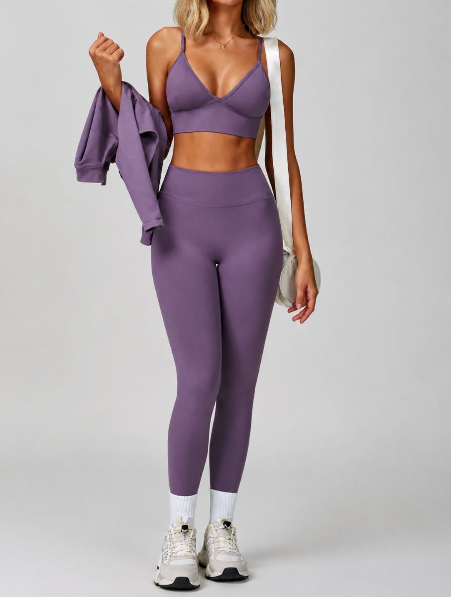 Woman wearing the ContourFlex Seamless Top & Leggings in Purple, standing in a relaxed pose while holding a jacket and carrying a shoulder bag.