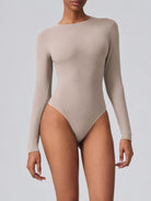 Woman wearing Aether Sculpting Long Sleeve Bodysuit in khaki, shown in a front pose with a sculpting fit.