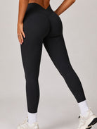Woman wearing the ContourFlex Seamless Top & Leggings in Black, posing at a back angle with one hand resting on her thigh and one leg extended.
