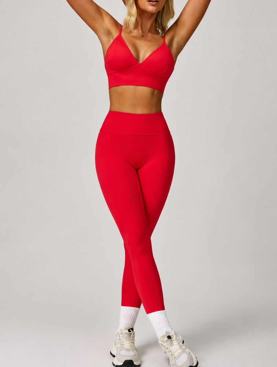 Woman wearing the ContourFlex Seamless Top & Leggings in Red, standing with arms raised and legs crossed in a front-facing pose.