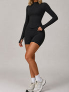 Side view of a woman wearing the ContourFlex Three-Piece Set in black, featuring a fitted zipped jacket and shorts, posing with one hand on her hip.