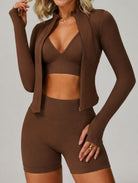 Front view of a woman wearing the ContourFlex Three-Piece Set in dark coffee, featuring a sports bra, fitted jacket, and shorts, posing with one hand raised near her shoulder.