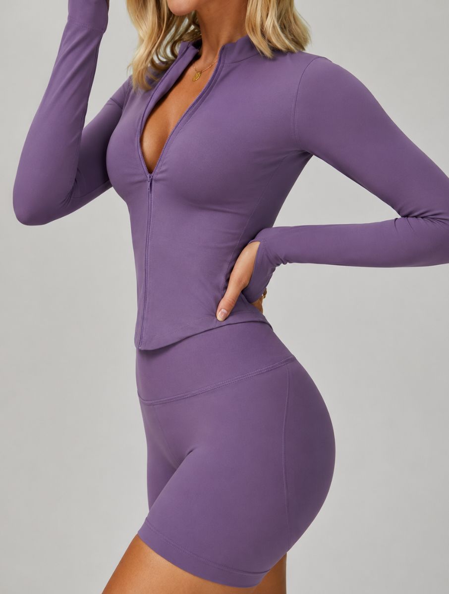 Side view of a woman wearing the ContourFlex Three-Piece Set in purple, featuring a fitted jacket and shorts, posing with one hand on her hip.